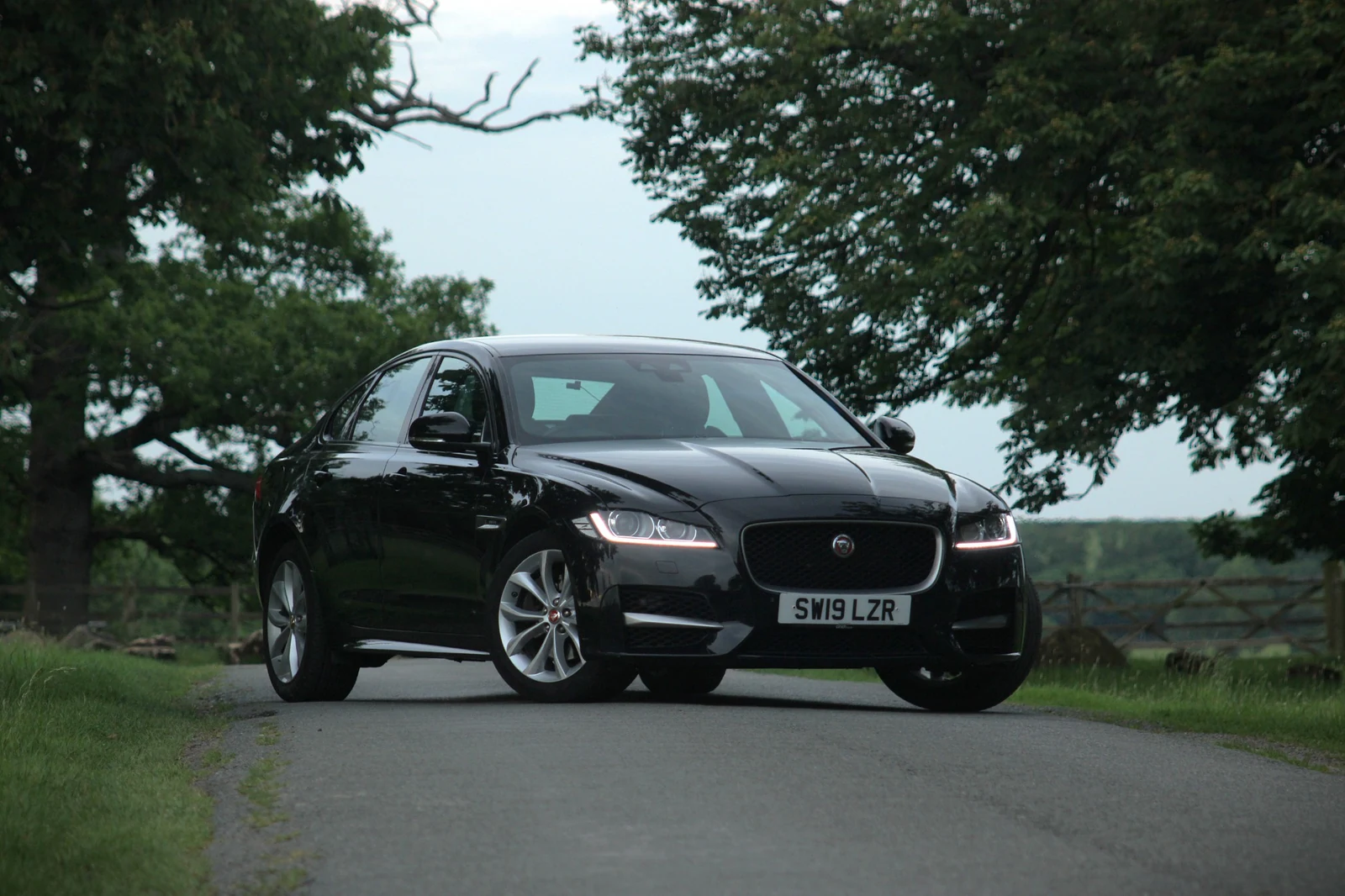 A low front three-quarter view of a black Jaguar parked on a drive beside trees.