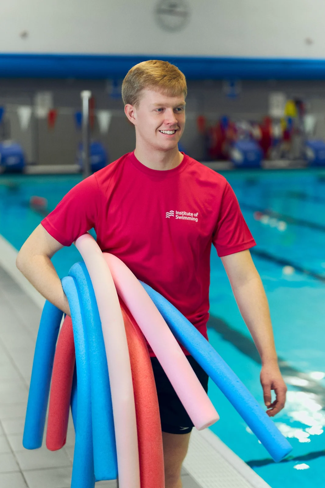 Jack Ruddle holding colourful swimming noodles beside the pool.